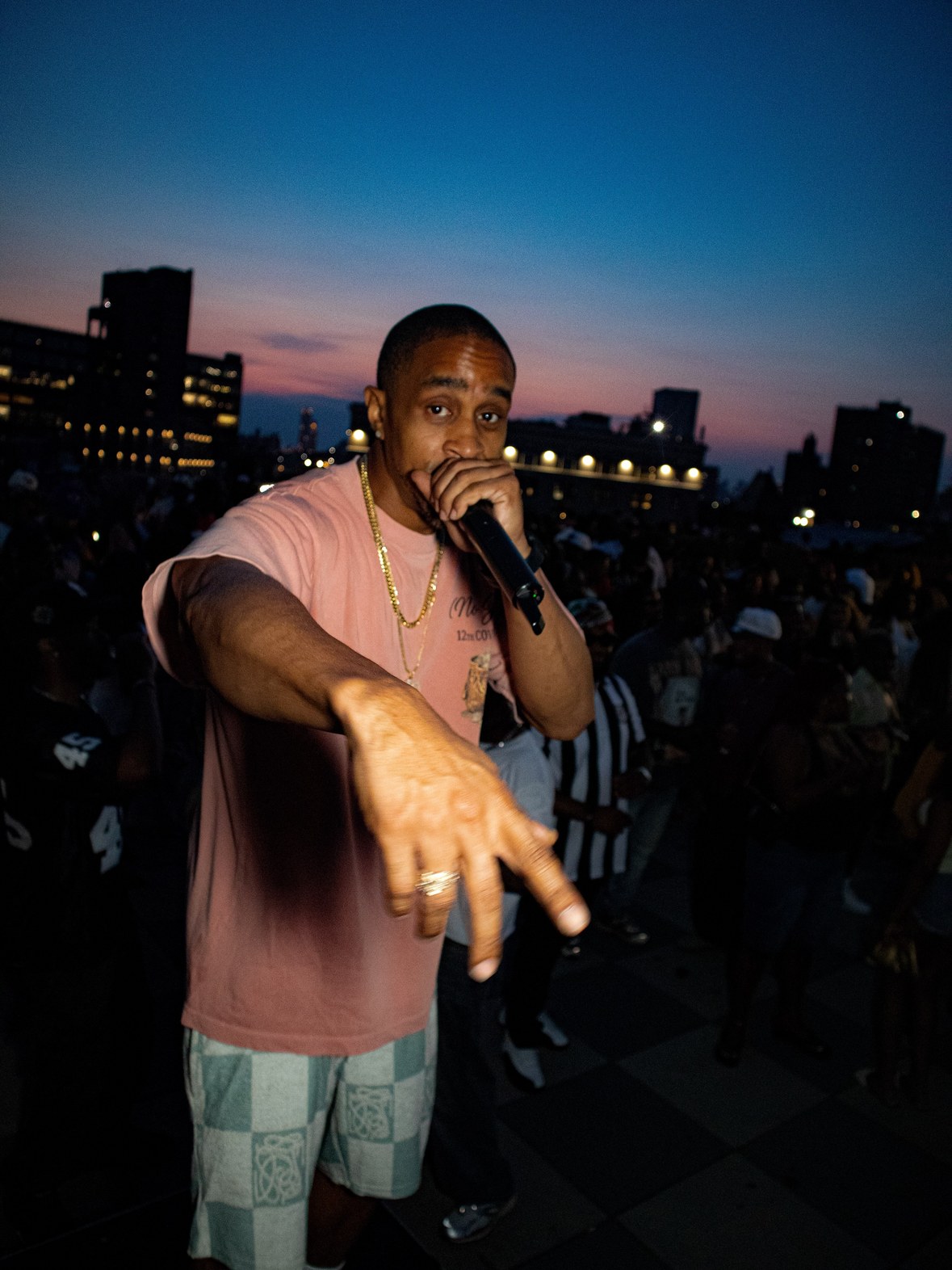 DJ Takeova on the microphone in front of a packed rooftop crowd at sunset