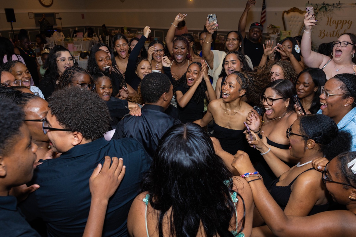 Birthday party guests cheering, laughing and filming on a packed dance floor